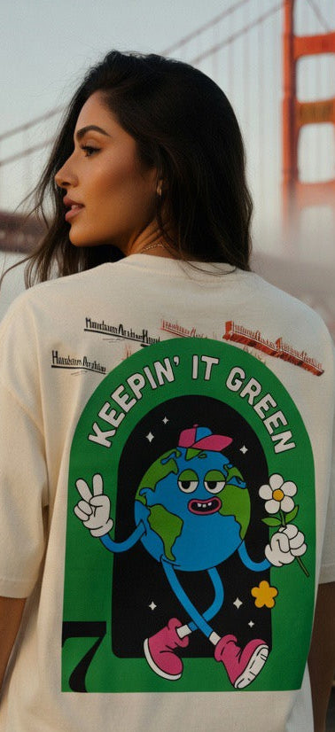 Cream crewneck T-shirt showing back graphic with a green globe character and the phrase “Keepin’ It Green”.